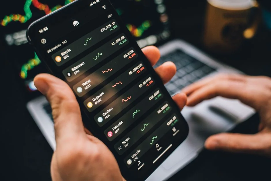 Hands holding smartphone with stock app, laptop displaying charts. Perfect for financial and technology themes.